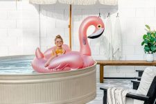 a fun and cool pool space with a stock tank pool, a flamingo float, an umbrella, a bench and a lounger is super chic