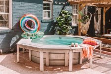 a funny and welcoming backyard pool space with a stock tank pool, a deck around, colorful floats and pillows and cushions around