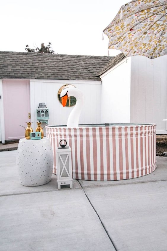 a funny backyard pool space with a striped stock tank pool, a side table with pineapple decor, candle lanterns and a float