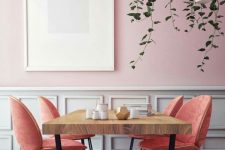 a gorgeous dining space with a pink and white panel wall, a wooden dining table, salmon pink chairs and suspended potted plants