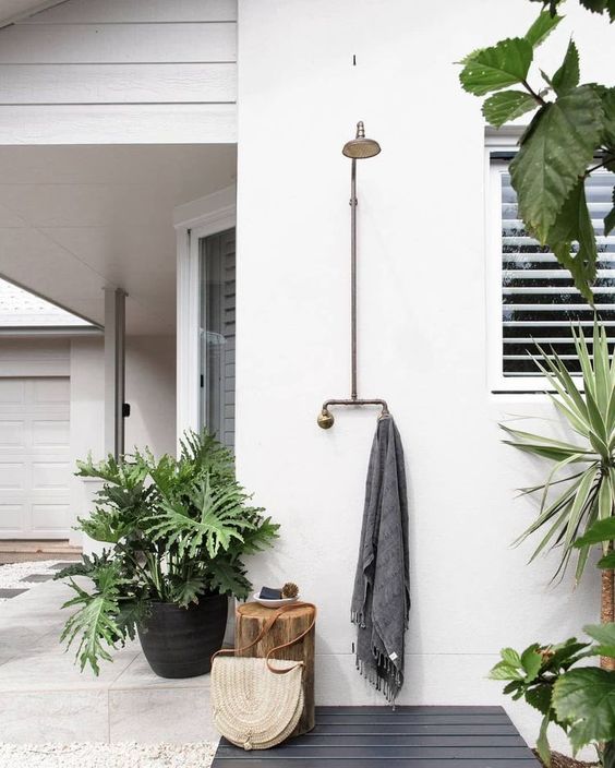a little and lovely outdoor shower space with a grey wooden deck and a towel, potted plants and a tree stump as a stool
