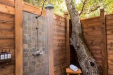 a lively outdoor shower space clad with planked wood, with a mosaic tile wall, a growing tree right here and a small stool