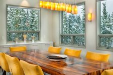 a lovely contemporary dining space with a long table, mustard chairs, a catchy pendant lamp and a view