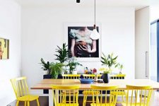 a lovely dining room with a navy sideboard, a wooden table, yellow chairs and a bench, lots of potted plants