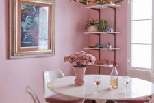 a lovely dining room with pink walls, an open shelving units, a round table and mauve chairs, a catchy black and gold chandelier