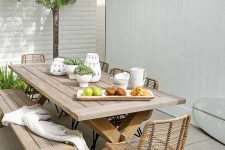 a lovely modern farmhouse dining space with a trestle table, a matching bench and some rattan chairs, greenery around and on the table