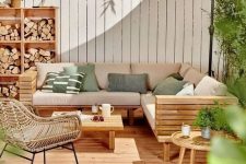 a lovely modern terrace with a wooden deck, a planked sofa and a table, a rattan chair, a storage unit with firewood