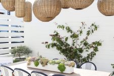 a lovely outdoor dining space with a whole cluster of pendant lamps, a long table and cool coastal chairs plus potted plants
