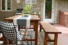 a lovely outdoor dining space with simple planked furniture, a striped runner, an umbrella and some greenery around