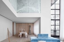 a luxurious minimalist space with stone panels, hardwood floors, double height windows, a blue sofa, a round side table is chic