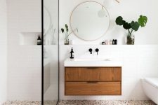 a mid-century modern bathroom with white walls and a bright terrazzo floor, a floating vanity and a round mirror, a pretty lamp and greenery