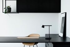 a minimalist home office with a black storage unit and shelf, a black desk and storage cabinets, a plywood chair and a table lamp