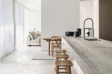 a minimalist kitchen with an oversized stone kitchen island and wooden stools plus all white walls around is chic