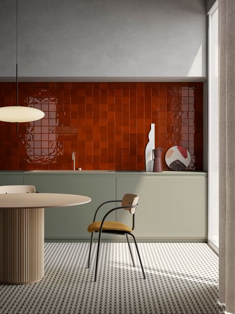 a minimalist kitchen with color - a hot red tile backsplash, sleek olive green cabinets, a curved table and chair plus a mosaic floor