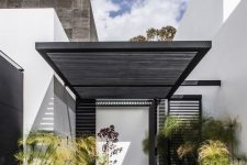 a modern front yard clad with dark tiles, with grass and tall plants and with a planked roof over the porch is very stylish and bold