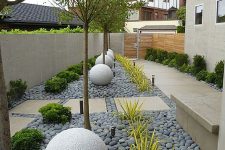 a modern front yard styled with tiles and grey pebbles, stone balls, trees, greenery and succulents is a stylish space that catches an eye