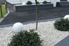 a modern front yard with a dark deck and neutral pebbles, greenery, trees and white balls plus elegant modern planters is a chic idea