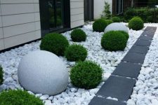 a modern front yard with large rocks and dark tiles for a contrast, greenery balls and oversized stone ones for bold landscaping