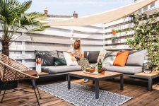 a modern summer deck with a built-in sectional, bold and printed pillows, potted plants and a round chair is a welcoming space to be