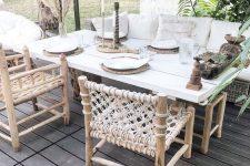 a neutral boho dining space with a wicker sofa and woven chairs, a simple table, potted greenery and pampas grass and woven placemats