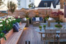 a peaceful rooftop terrace with a wooden deck, built-in furniture, a lovely wooden dining set, potted blooms and plants