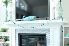 a pretty coastal mantel with a turquoise whale, green vases, a pompom garland in blues and a whitewashed driftwood star