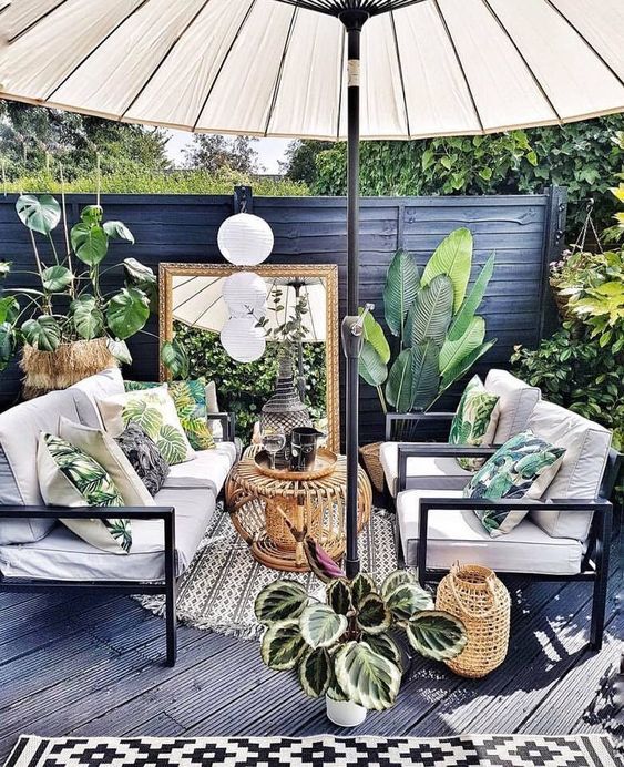 a pretty summer terrace with a black deck, elegant garden furniture, a rattan table, candle lanterns, an umbrella and potted plants