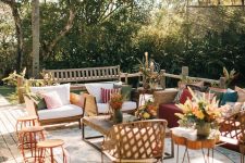 a pretty summer terrace with a wooden deck, modern wicker furniture, potted plants and blooms, a wood slice table and printed rugs