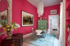 a quirky dining room with hot pink walls, a round metal table, a mirror in an ornated frame, blooms and a catchy chandelier