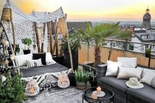 a refined boho rooftop terrace with chic sofas and a daybed, printed pillows, potted greenery and a palm tree and some lanterns