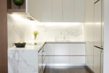 a refined minimalist kitchen with sleek white cabinets, a white marble backsplash and waterfall countertop, built-in lights and open storage compartments