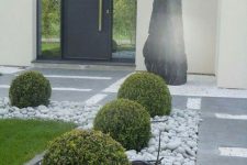a refined modern front yard with stone tiles and rocks, with grass and elegant greenery balls looks chic and ultimate and inspires