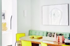 a retro-inspired dining space with light blue walls, a curved table, a green upholstered sofa, yellow chairs and a cool mosaic floor
