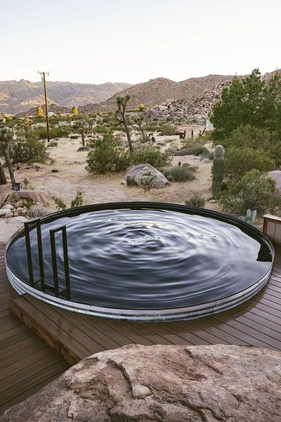 a round pool made of a stock tank, with a ladder and a wooden deck around it plus a view of the desert is a lovely space to spend time