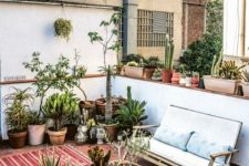 a simple modern summer patio with layered rugs, a round wooden table, some modern furniture and lots of potted plants and cacti