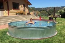 a simple stock tank pool placed on the grass is a perfect solution for a hot and sunny summer day to chill in your backyard