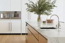 a sleek and refined minimalist kitchen with white cabinets and a waterfall countertop kitchen island, neutral fixtures and greenery