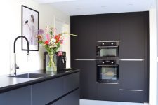 a sleek black kitchen with black countertops and fixtures, with artworks and some bright blooms is a chic and bold space