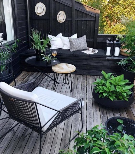 a small Scandinavian deck with a built in black daybed, a white chair, mini round tables, potted plants and candle lanterns