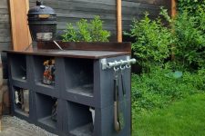 a small Scandinavian outdoor kitchen of cinder blocks painted black, with a grill and lots of greenery around for a fresh feel