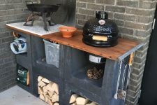 a small and comfy outdoor kitchen of black cinder blocks, with firewood, a grill and a cooker with a pan is amazing