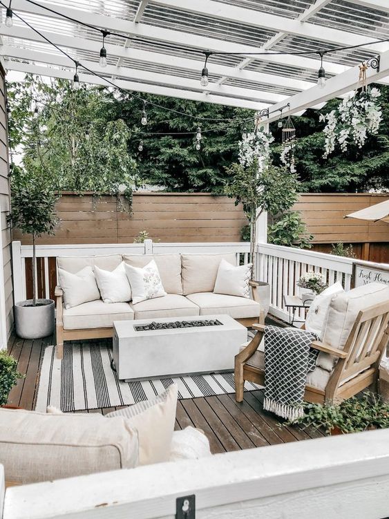 a small and cozy deck with neutral furniture, a fireplace, potted plants and printed textiles everywhere is a chic space