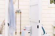 a small and cozy outdoor shower with planked wooden walls and a wooden bath mat plus printed textiles and a basket with eveyrthing necessary