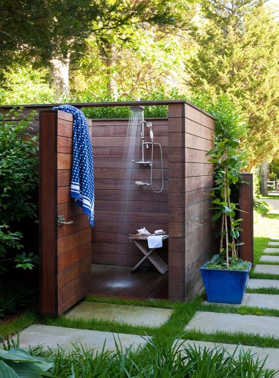 a small and private outdoor shower fully clad with stained wood and with walls, with a small stool and printed towels