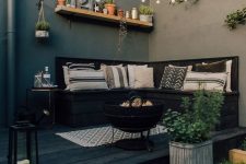 a small black deck with a built-in seat and printed pillows, string lights over the space, potted plants and candle lanterns