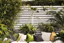 a small deck surrounded with greenery, with a green pallet daybed, a pallet coffee table and colorful pillows is welcoming