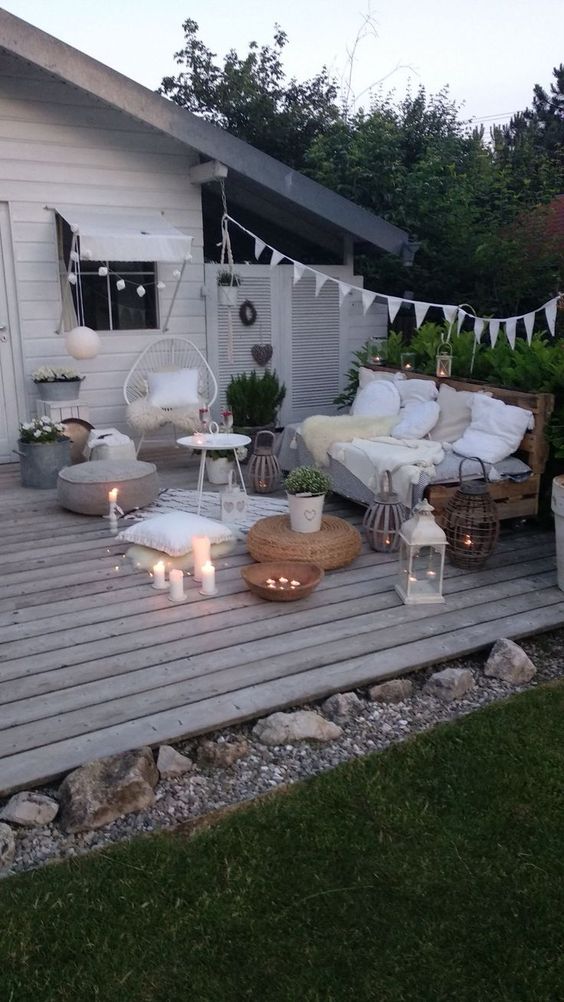 a small deck with an outdoor Scandinavian living room, pallet and rattan furniture, poufs and candles plus string lights