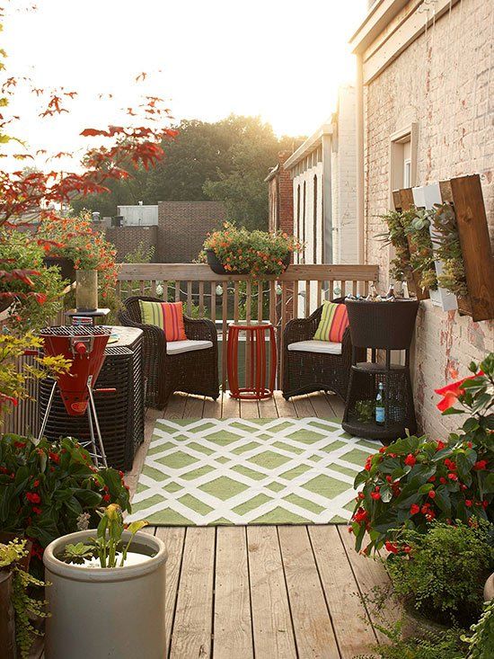 a small deck with potted blooms and plants, woven dark furniture, a bold rug and a mini pond plus a mini bar