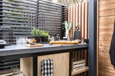 a small industrial and rustic outdoor kitchen with an open and closed storage unit, a concrete countertop, a planked wall and potted herbs