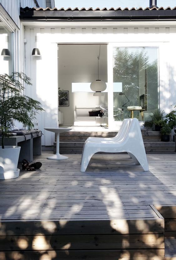 a small minimalist deck with a bench with cushions, white loungers, a coffee table, potted plants is a chic and cool space